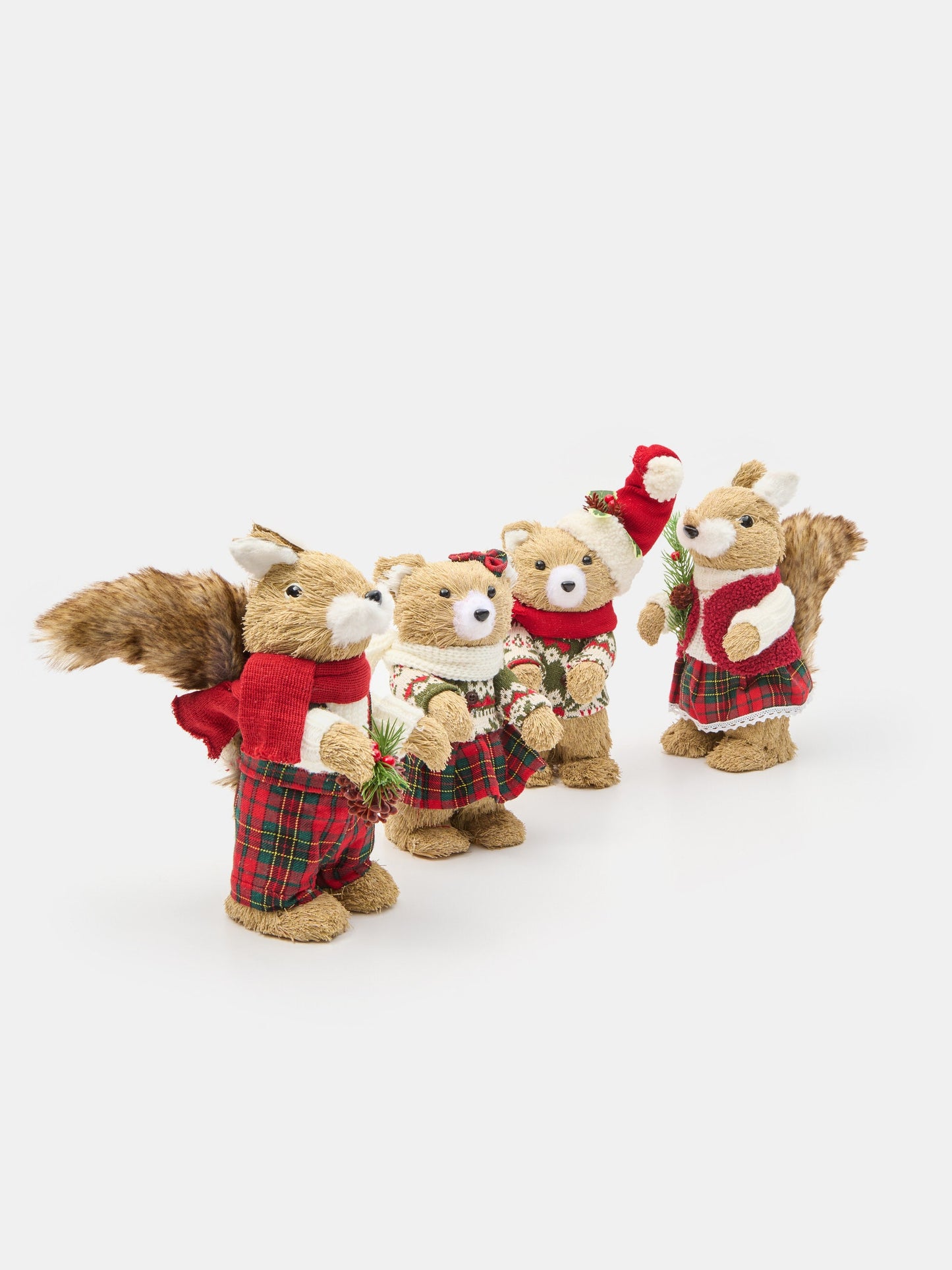 Four plush toy squirrels dressed in festive Christmas clothing, including red plaid skirts, scarves, and hats, arranged on a light gray background.