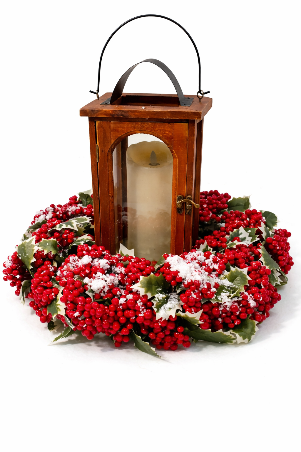 A rustic wooden lantern with a black metal handle sits centered on a festive holiday wreath made of red berries, green holly leaves, and white snow-like dusting, isolated on a white background.
