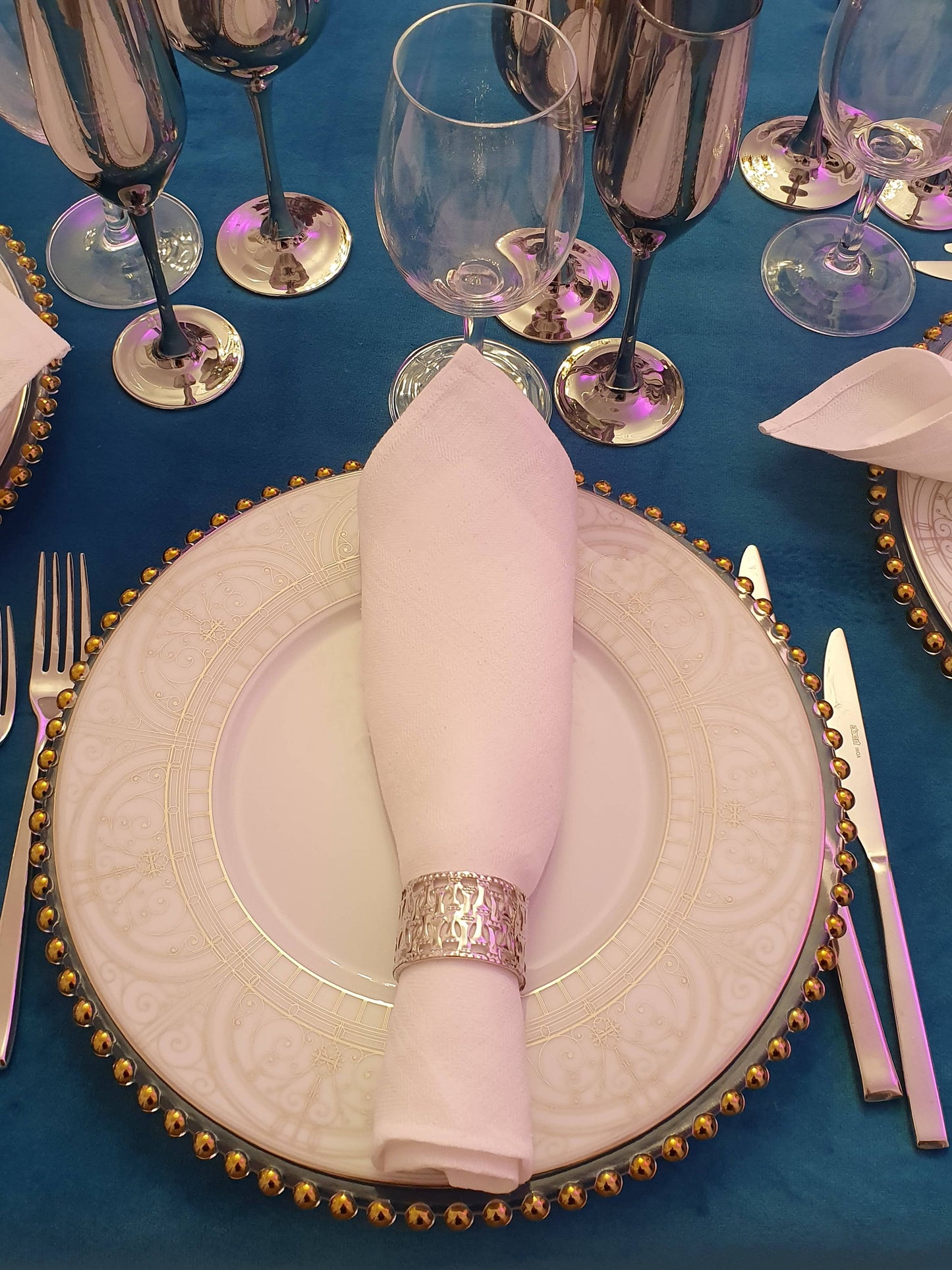 Elegant table setting with gold-rimmed plates, silverware, and a blue tablecloth for rent 7skyrent