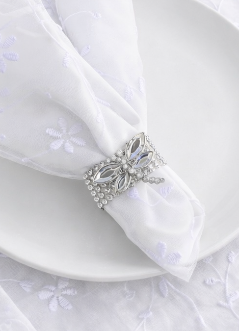 White plate with folded napkin and decorative brooch on a textured white background