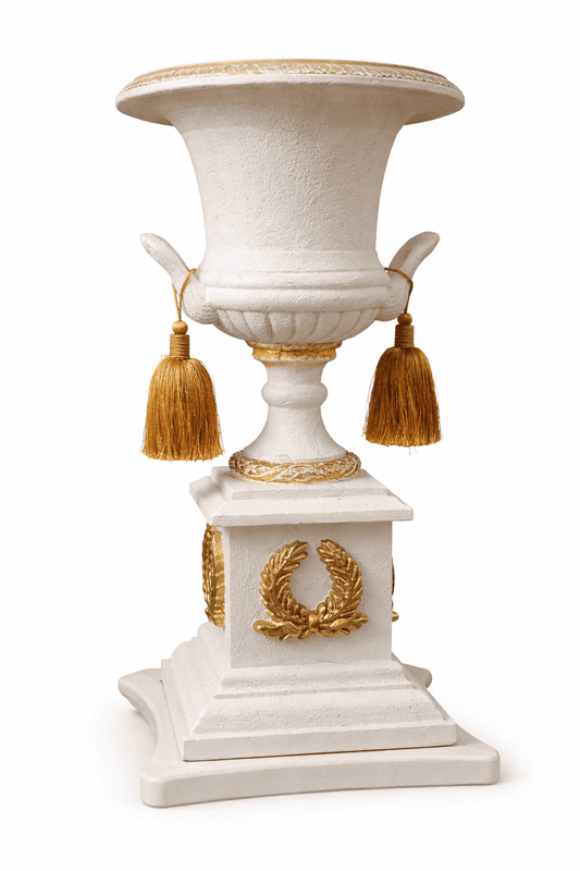 White and gold neoclassical decorative urn vase with laurel wreath ornament and removable tassels on pedestal base.