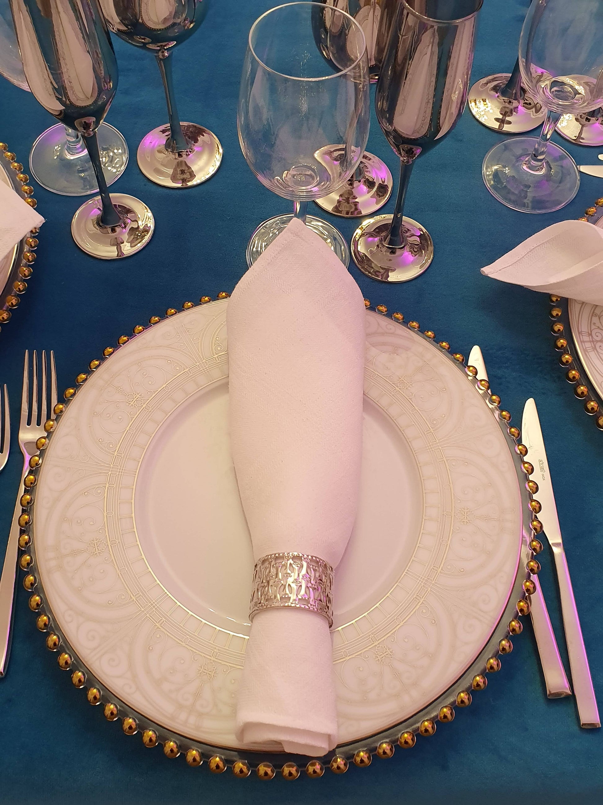 Elegant table setting with gold-rimmed plates, silverware, and a blue tablecloth for rent 7skyrent